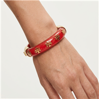 Tory Burch Kira glossy red resin bangle bracelet with repeating gold tone T logo charms, gold hardware, 2.25 inch diameter, and 0.5 inch width.