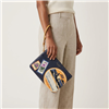 Tory Burch Perry leather wristlet in Royal Navy and Daylily with colorful vintage aviation patches, airplane graphics, floral travel stamps, first cabin baggage artwork, gold tone hardware, and wrist strap.