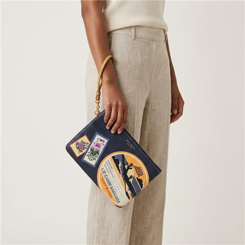 Tory Burch Perry leather wristlet in Royal Navy and Daylily with colorful vintage aviation patches, airplane graphics, floral travel stamps, first cabin baggage artwork, gold tone hardware, and wrist strap.