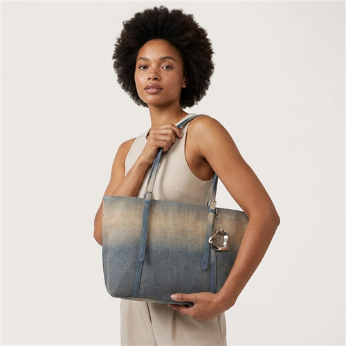 Betsey Johnson Slouchy Denim Tote Bag featuring blue and neutral ombre coloring, long shoulder handles, silver tone hardware, and a dimensional handbag charm.