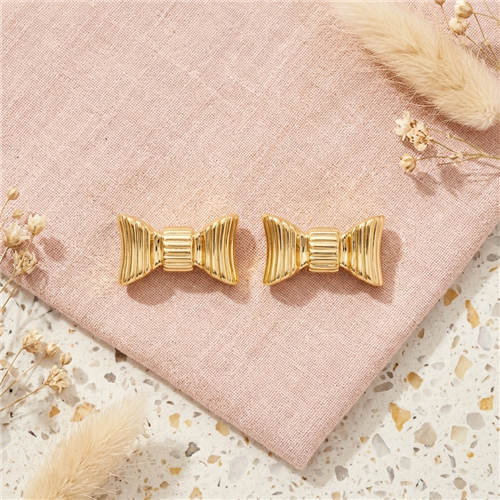 Kate Spade New York gold tone stud earrings featuring dimensional sculpted ribbon bow shapes with polished ridged detailing.
