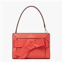 Kate Spade red wristlet clutch crafted from pebbled leather with patent leather trim, featuring a large asymmetrical bow applique, gold tone logo, top zip closure, short carry strap, and compact designer evening handbag silhouette.